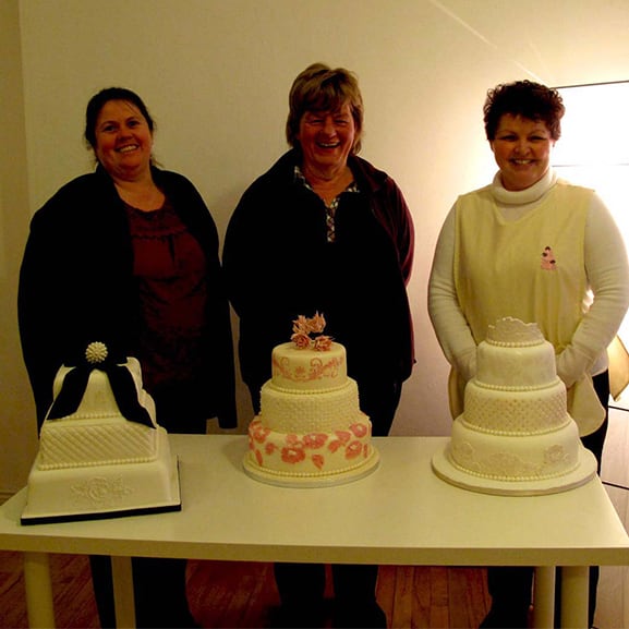 Three smiling woman with cakes in front of them